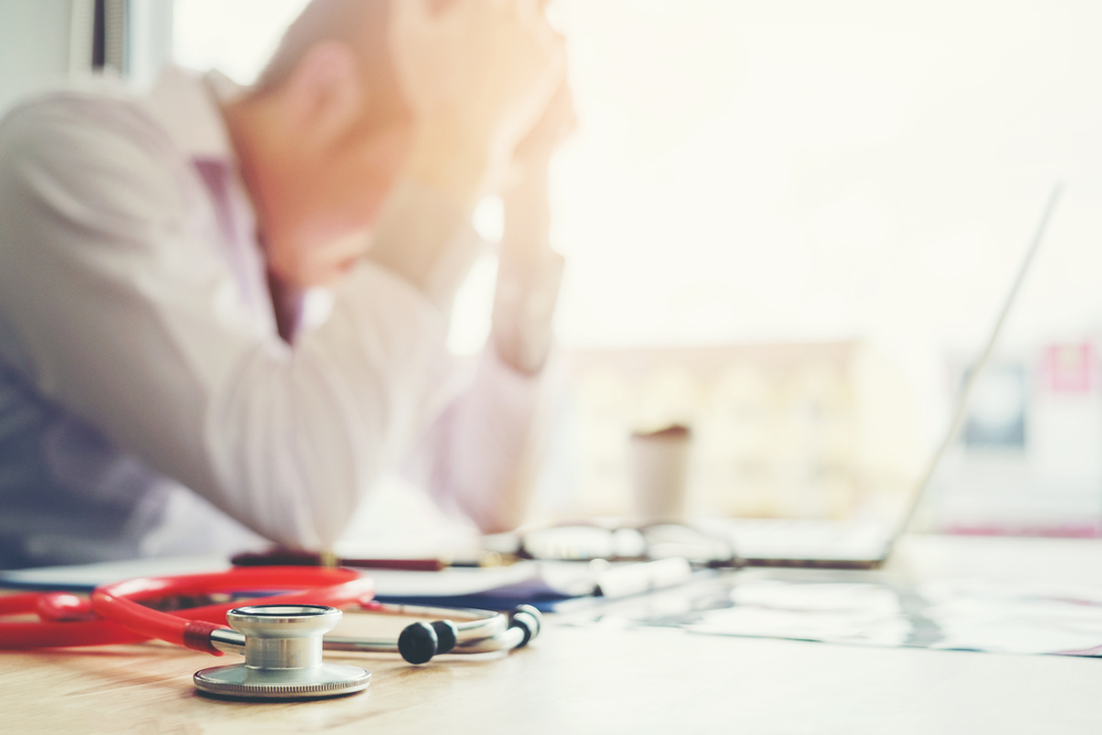 Stressed veterinarian sitting with laptop and stethoscope, head in hand at work